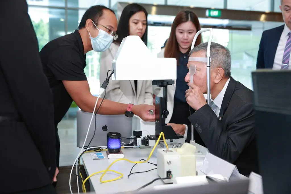 Dr Vivian Balakrishnan seated at an early AVAT rig in 2023, his head held in the rest while a Digital Life Line team member adjusts the device — photograph by NUS Medicine